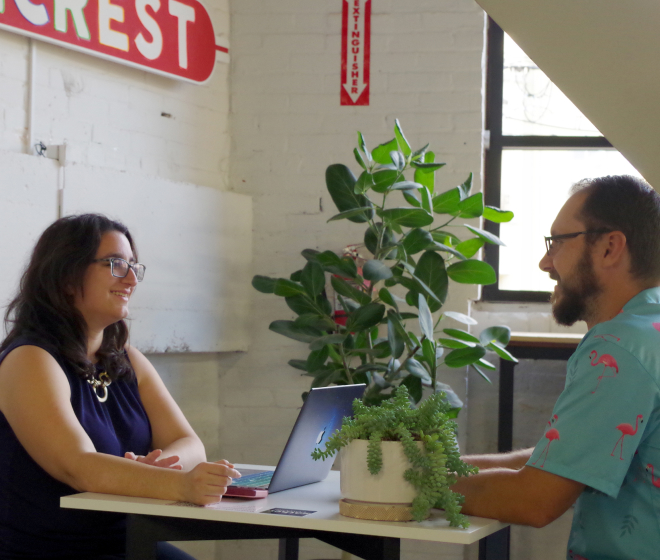 A man and woman sitting at a table with a laptop, working together on a project.