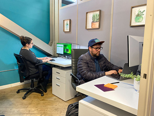 Two people sitting at desk typing in a small, dedicated office space at Cowork and Connect