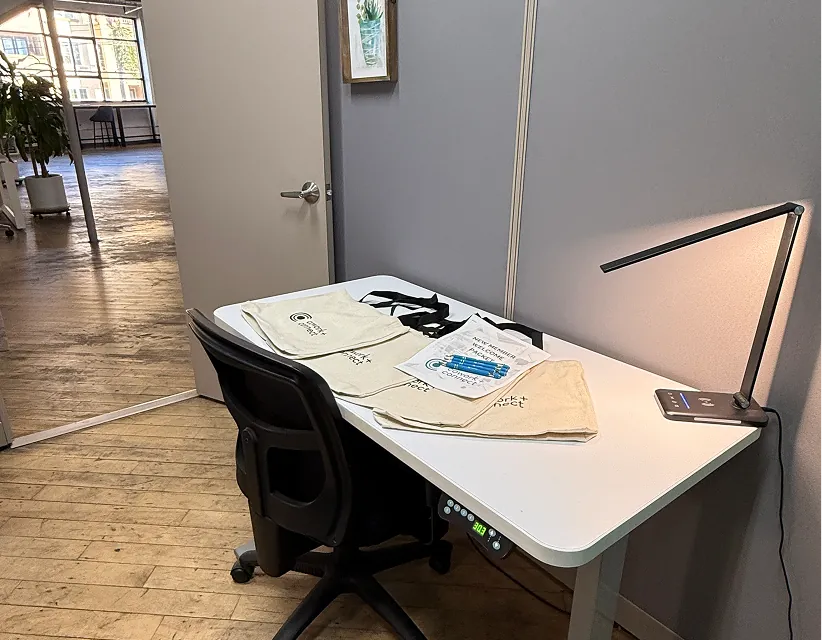 Modern office workspace with white desks, ergonomic chairs, and wood flooring, illuminated by soft natural light with wooden slat wall accents.