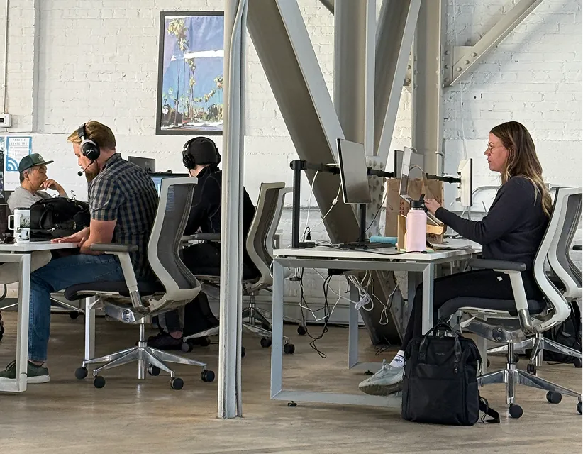 Team members work in a bright, industrial office with white brick walls. A worker wears HyperX headphones near a branded Alo water bottle.